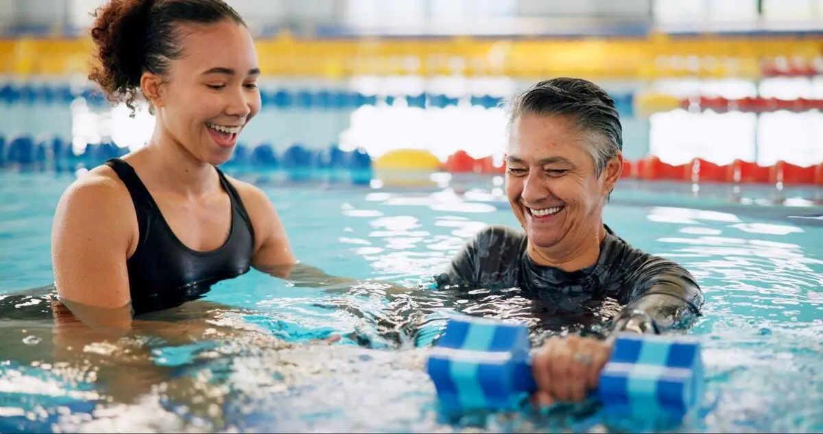Swimming instructor guiding an adult student with a kickboard in the pool