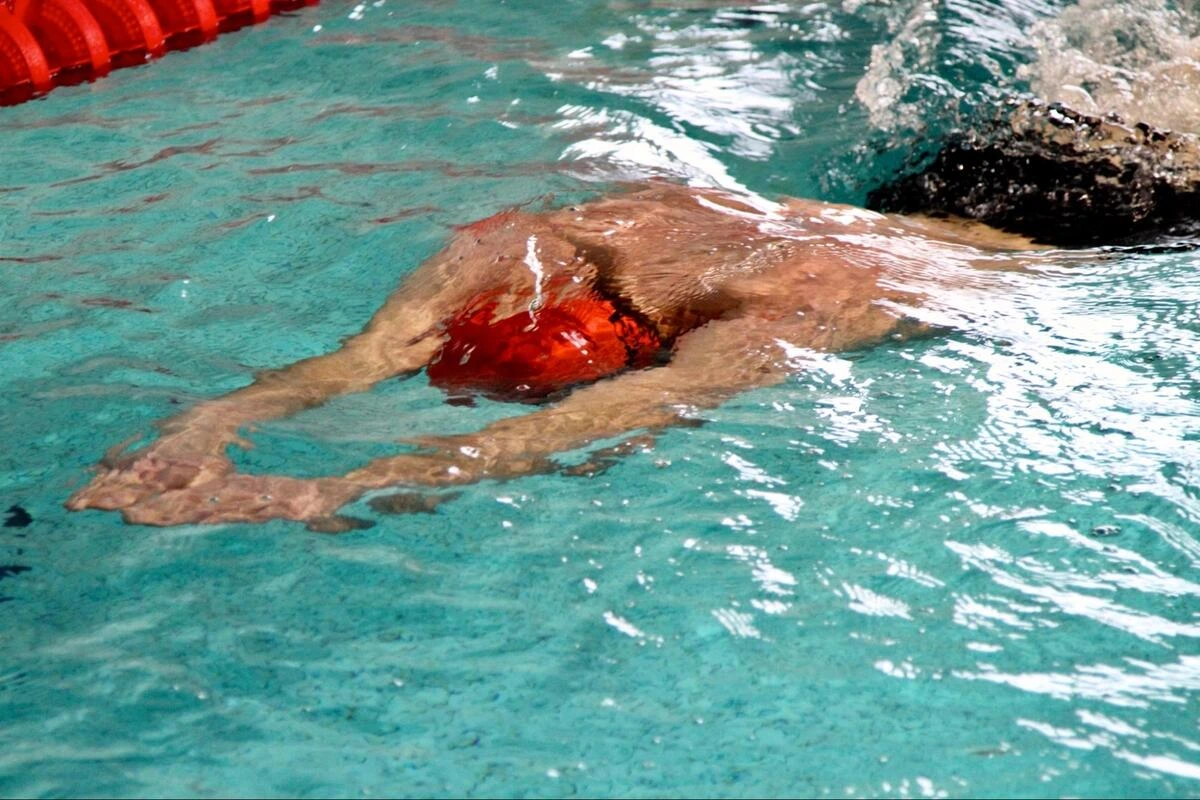Swimmer performing breaststroke in a pool with a lane rope in the background